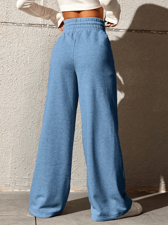 Woman wearing blue drawstring pleated wide leg pants with high waist and shirring detail against a textured wall.